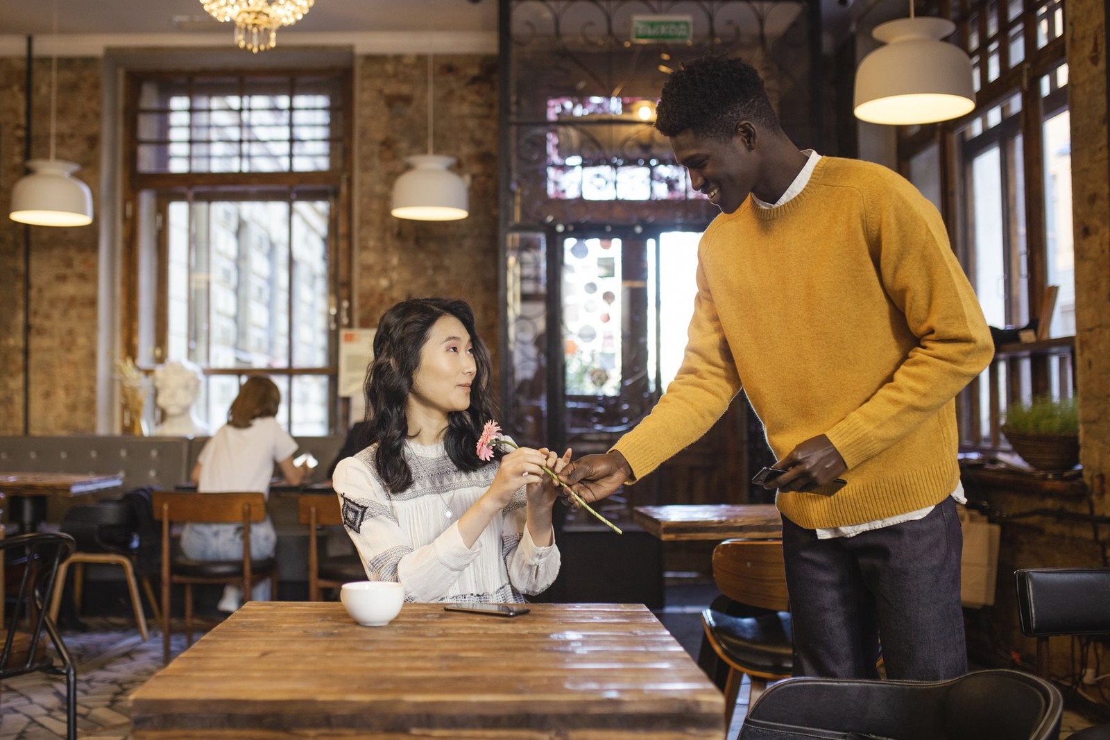 A man gives an Asian woman a flower during a cafe date