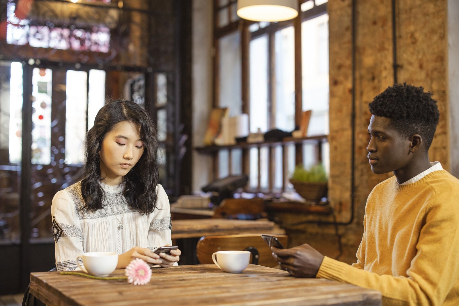 An Asian woman and her date looking at their phones across a cafe table
